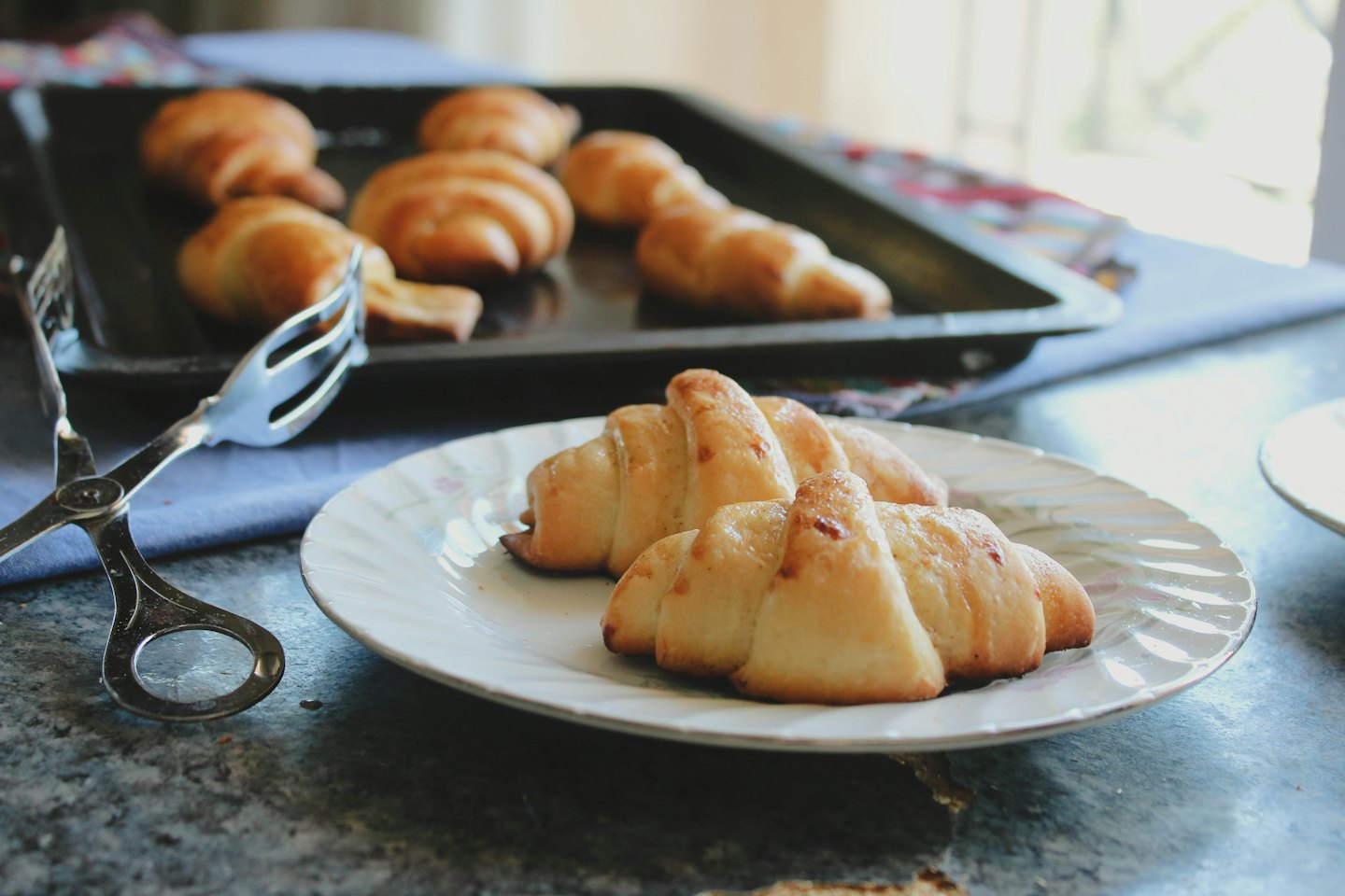 Two golden croissants on a white plate with tongs.